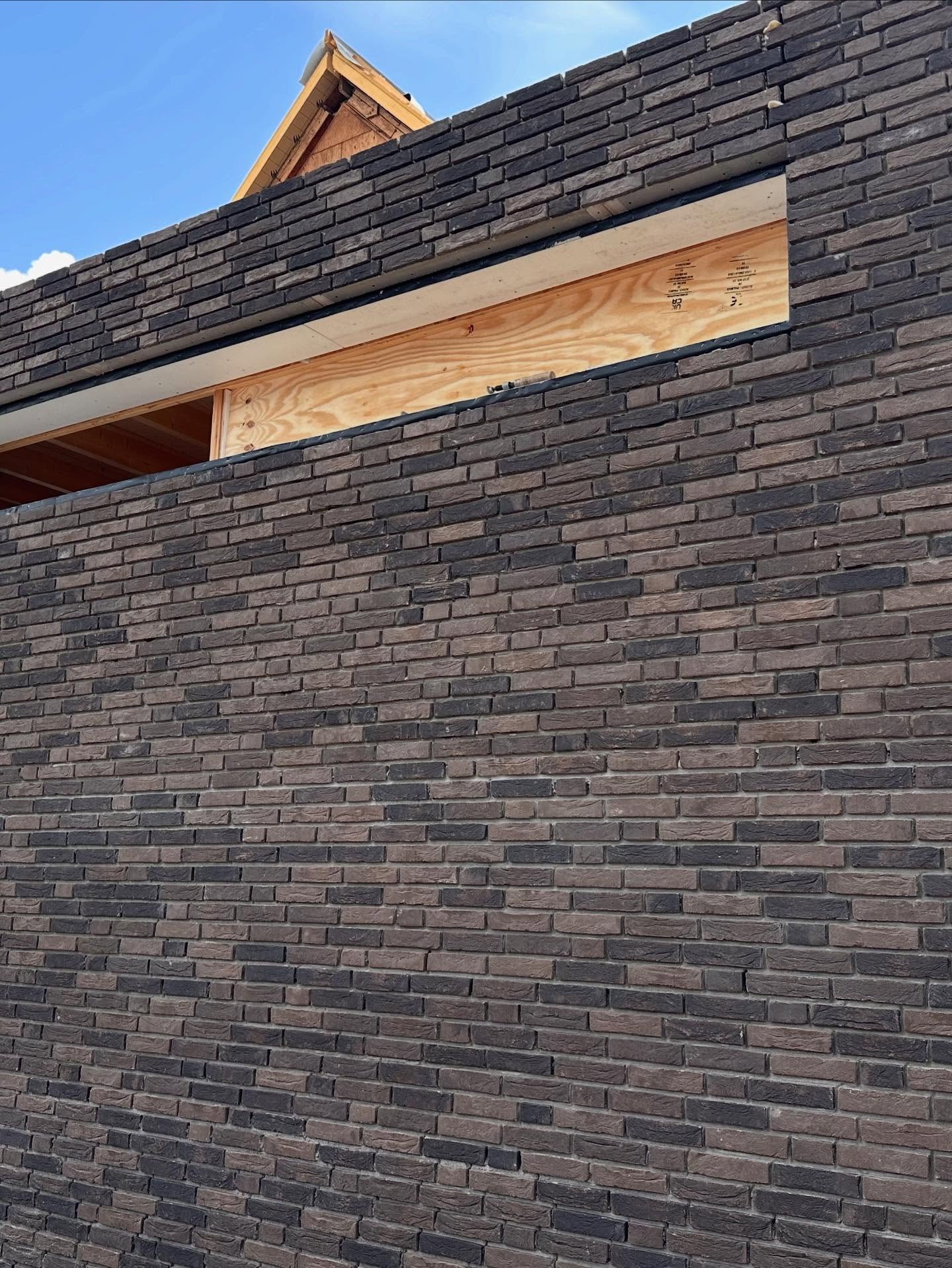 Aanbouw van donkere, bijna zwarte gevelsteen met een strakke lichte voeg en een houten latei boven de pui
