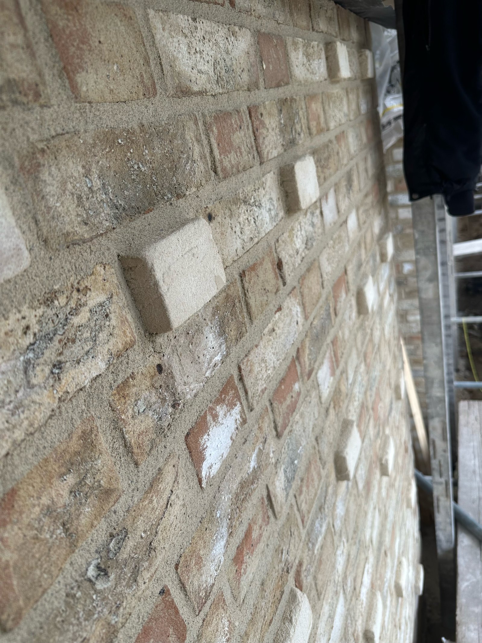 Close-up van een gevel met oude, gemengde stenen en lichte voegen in pointerwerk, met enkele witte koppen