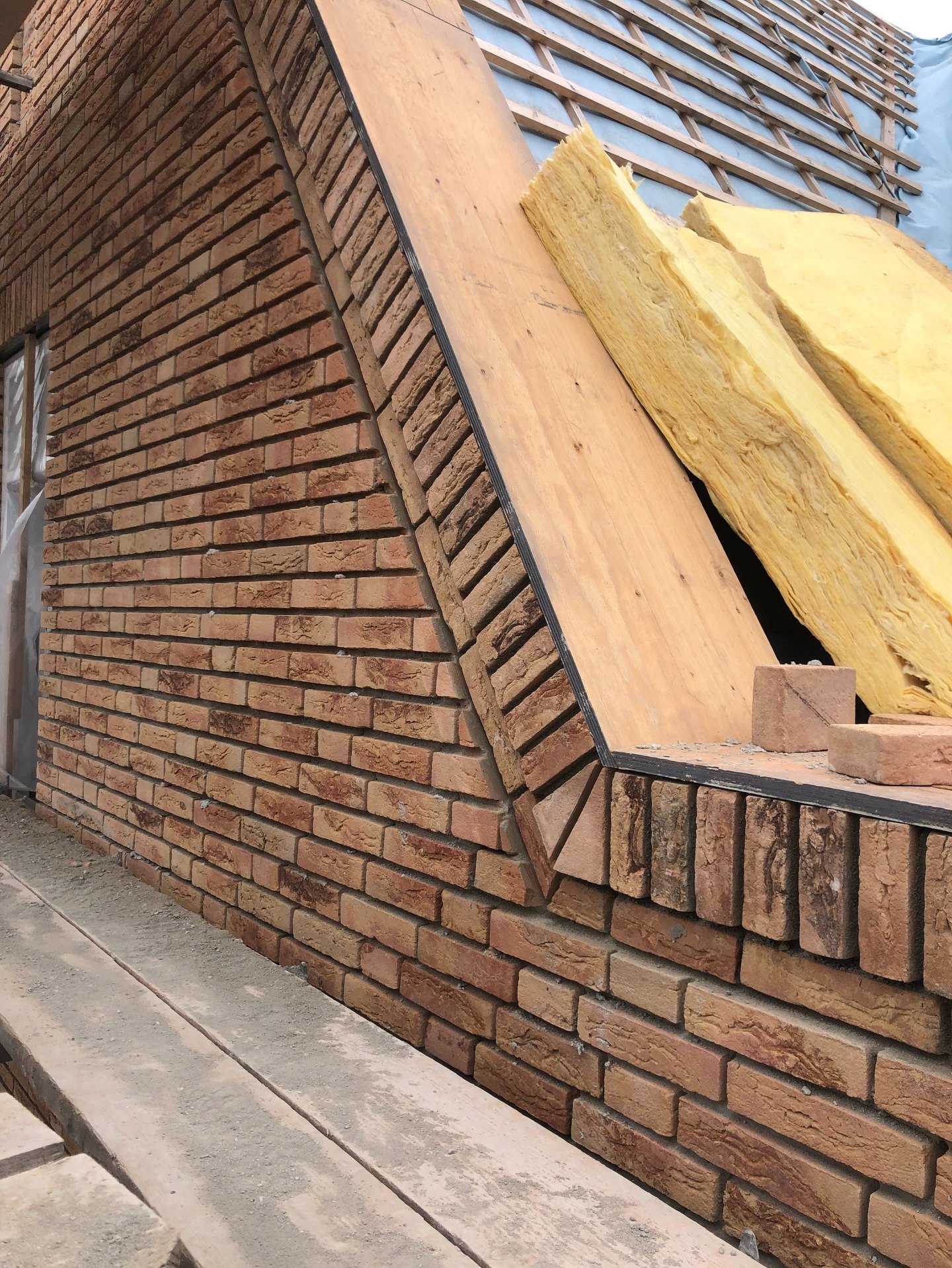 Topgevel van rode handvormsteen met een schuine rollaag langs het dakvlak, tijdens de bouw
