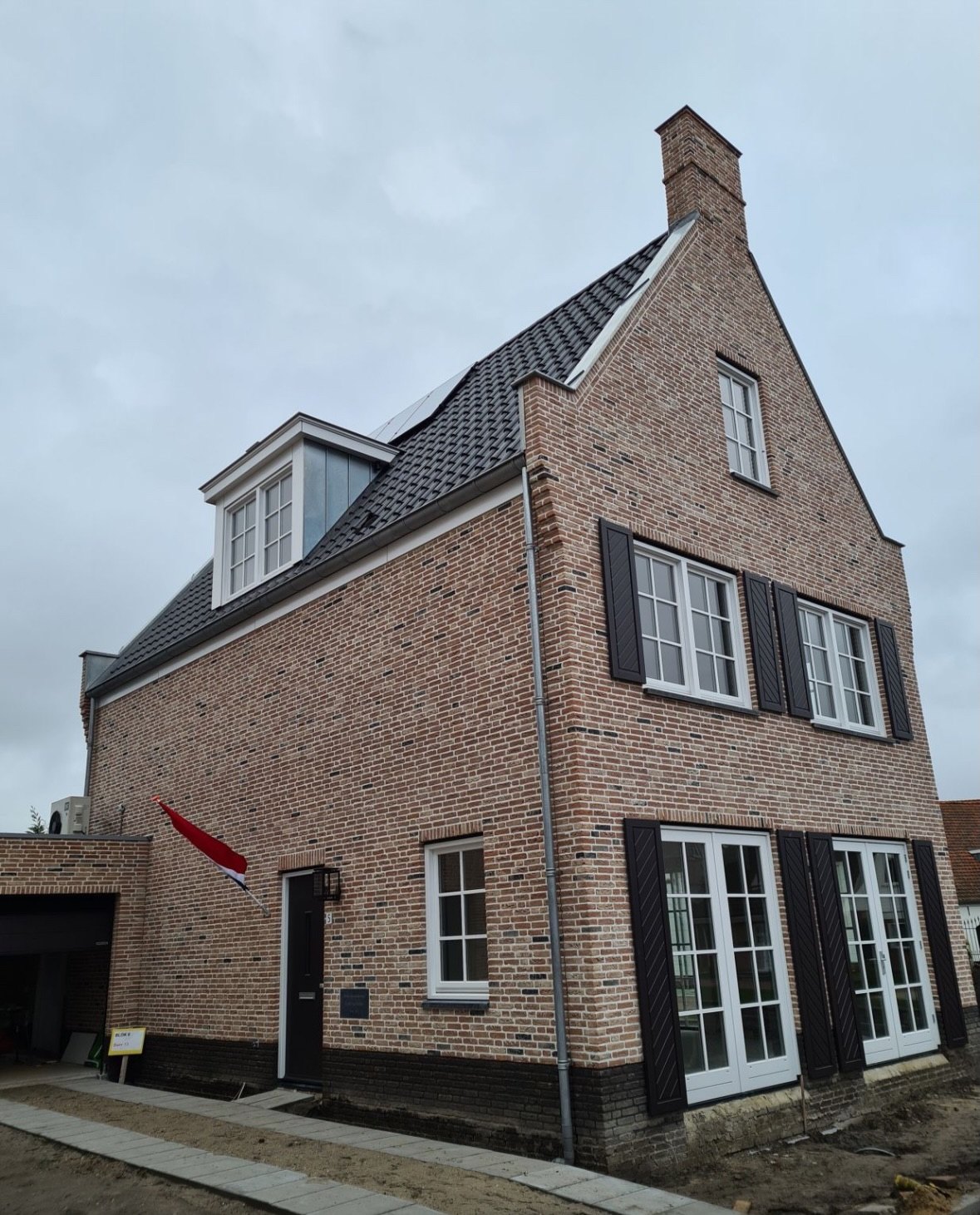 Woning van lichte gevelsteen met een topgevel en openslaande deuren, van achter gezien