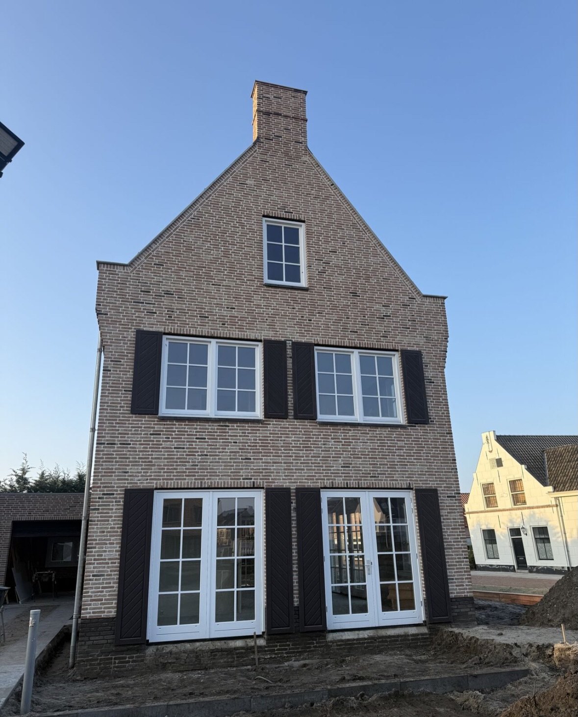 Nieuw gemetselde woning met een topgevel, witte kozijnen en donkerblauwe luiken